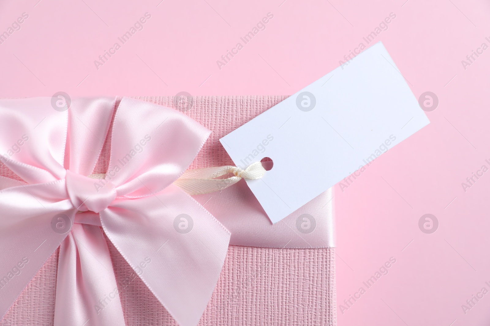 Photo of Gift box with blank tag on light pink background, closeup