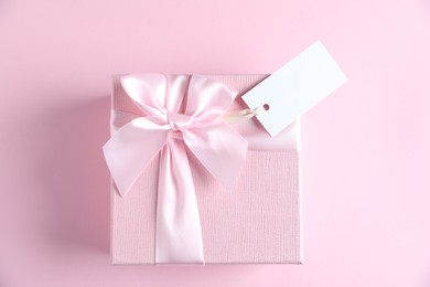 Photo of Gift box with blank tag on light pink background, top view