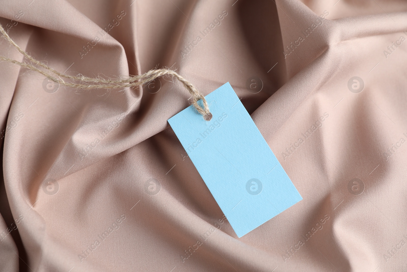 Photo of Blank tag with string on beige fabric, closeup