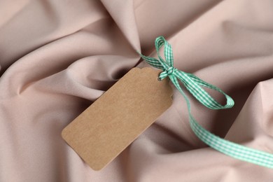 Photo of Blank tag with ribbon bow on beige fabric, top view