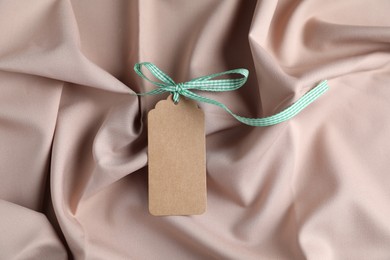 Photo of Blank tag with ribbon bow on beige fabric, top view