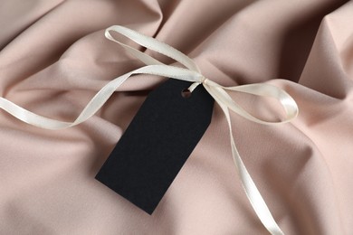 Photo of Blank tag with ribbon bow on beige fabric, top view