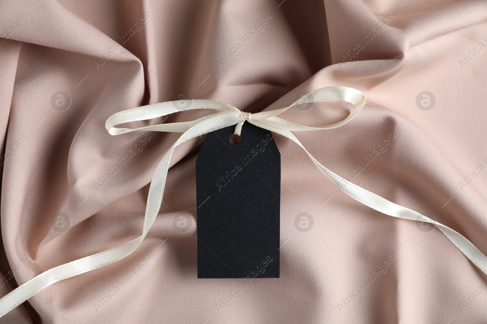 Photo of Blank tag with ribbon bow on beige fabric, top view