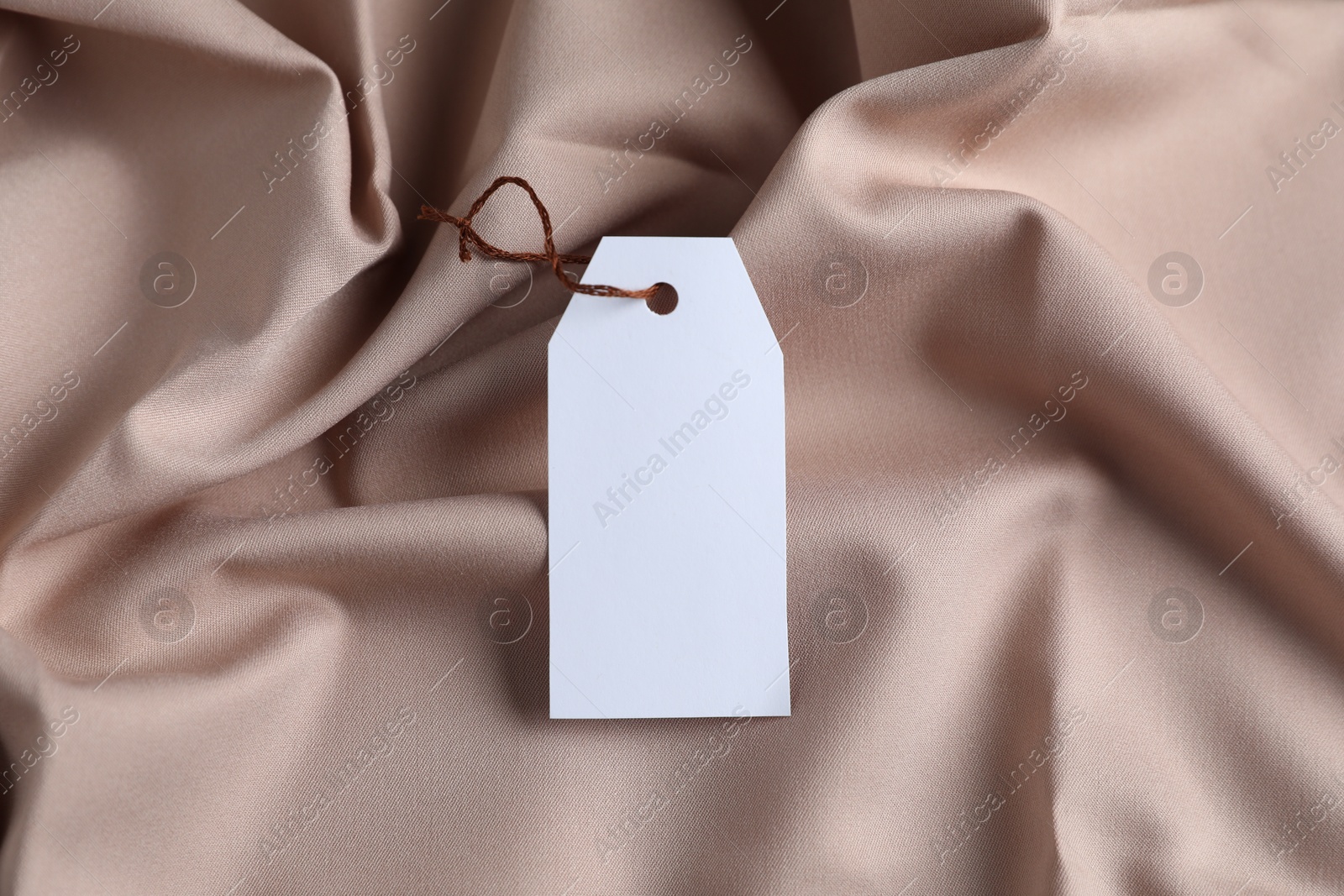 Photo of Blank tag with string on beige fabric, top view