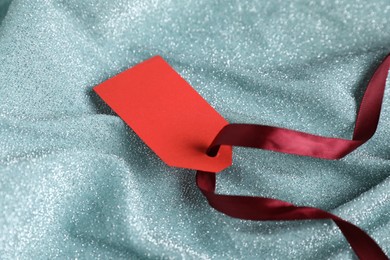 Photo of Blank tag with ribbon on teal fabric, closeup