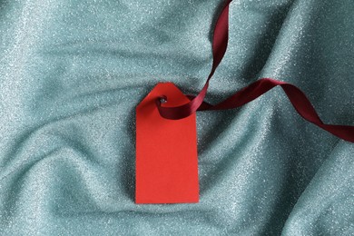 Photo of Blank tag with ribbon on teal fabric, top view