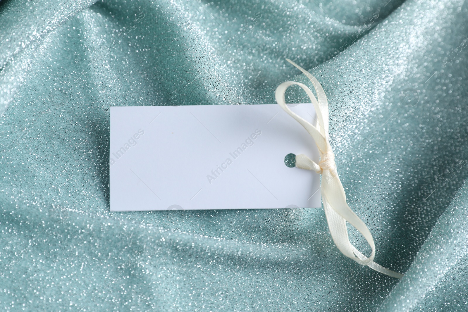 Photo of Blank tag with ribbon bow on teal fabric, closeup