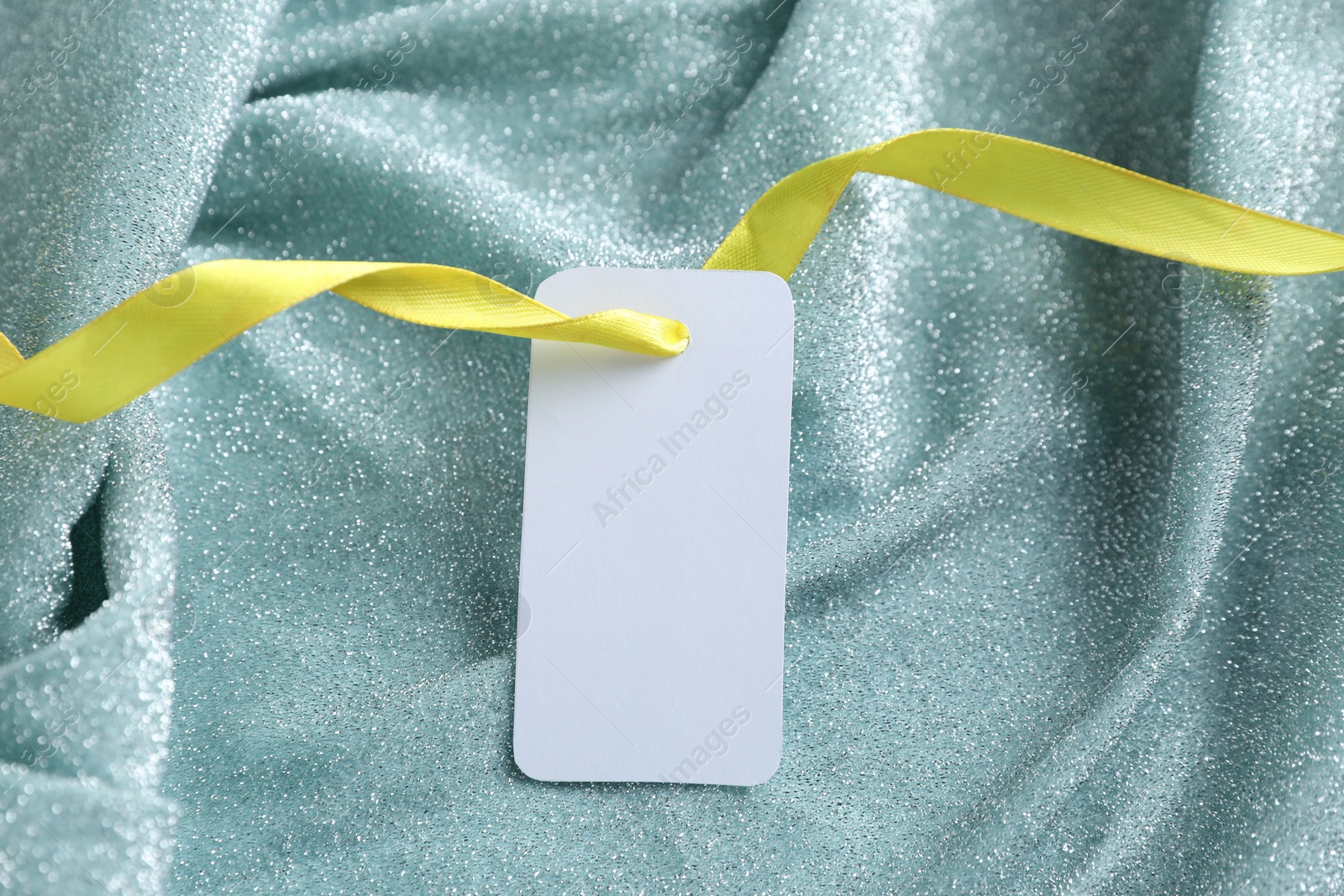 Photo of Blank tag with ribbon on teal fabric, closeup