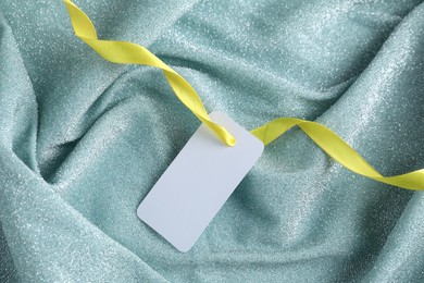 Photo of Blank tag with ribbon on teal fabric, top view