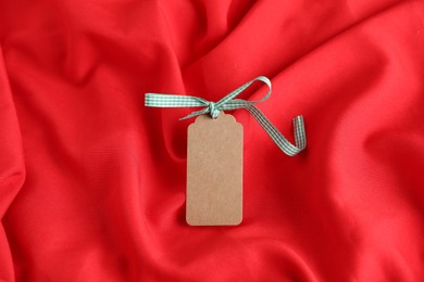 Photo of Blank tag with ribbon bow on red fabric, top view