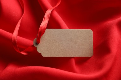 Photo of Blank tag with ribbon on red fabric, closeup