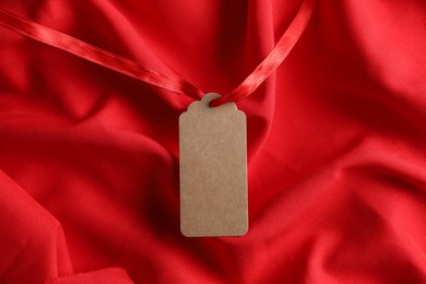 Photo of Blank tag with ribbon on red fabric, top view