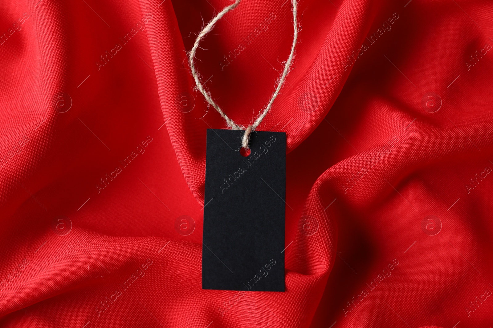 Photo of Blank tag with string on red fabric, top view