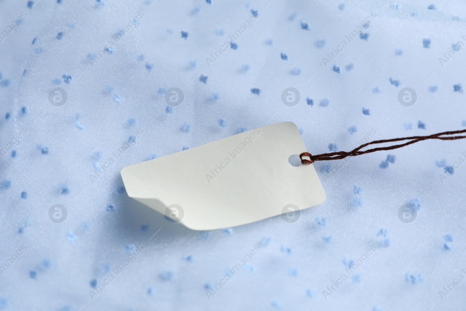 Photo of Blank tag with string on white fabric, closeup