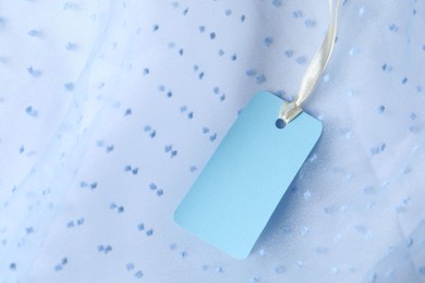 Photo of Blank tag with ribbon on white fabric, closeup