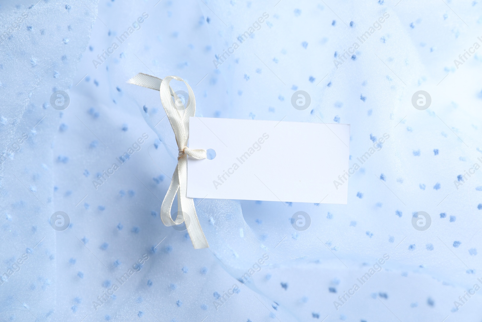 Photo of Blank tag with ribbon bow on white fabric, closeup