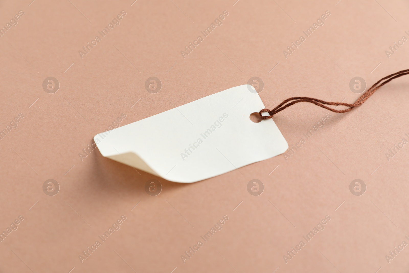 Photo of Blank tag with string on beige background, closeup