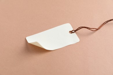 Photo of Blank tag with string on beige background, closeup