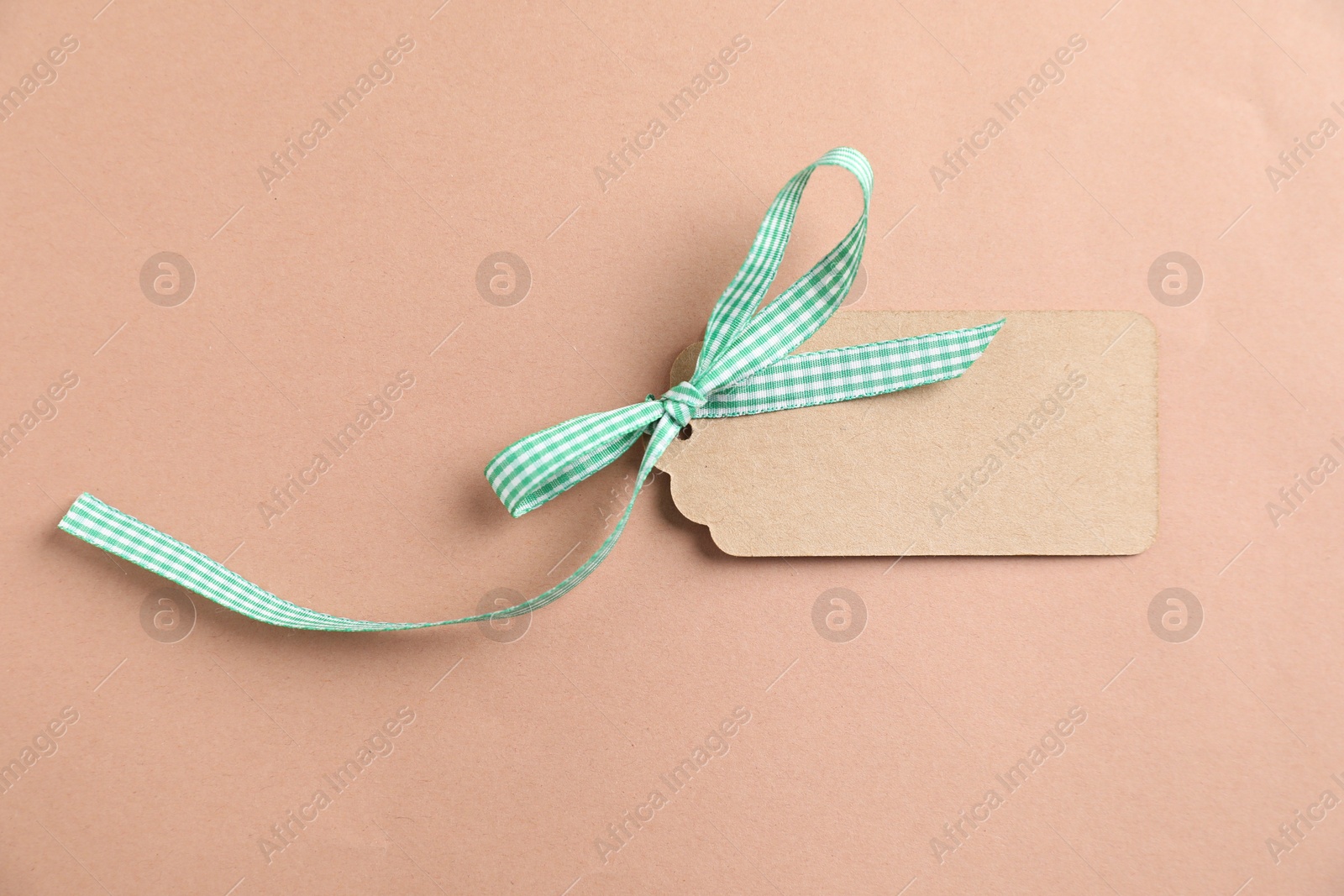 Photo of Blank tag with ribbon bow on beige background, top view