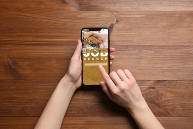 Image of Job search. Woman using employment website on mobile phone at wooden table, top view