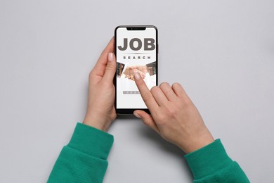 Image of Job search. Woman using employment website on mobile phone at grey table, top view