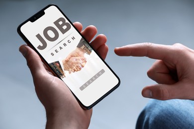 Image of Job search. Man using employment website on mobile phone on grey background, closeup