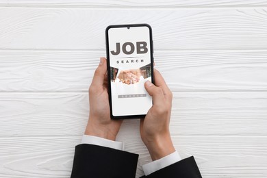 Image of Job search. Woman using employment website on mobile phone at white wooden table, top view