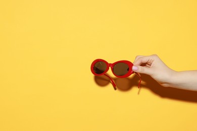 Photo of Woman with beautiful sunglasses on orange background, closeup and space for text. Stylish accessory