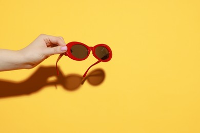 Photo of Woman with beautiful sunglasses on orange background, closeup and space for text. Stylish accessory