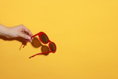 Photo of Woman with beautiful sunglasses on orange background, closeup and space for text. Stylish accessory