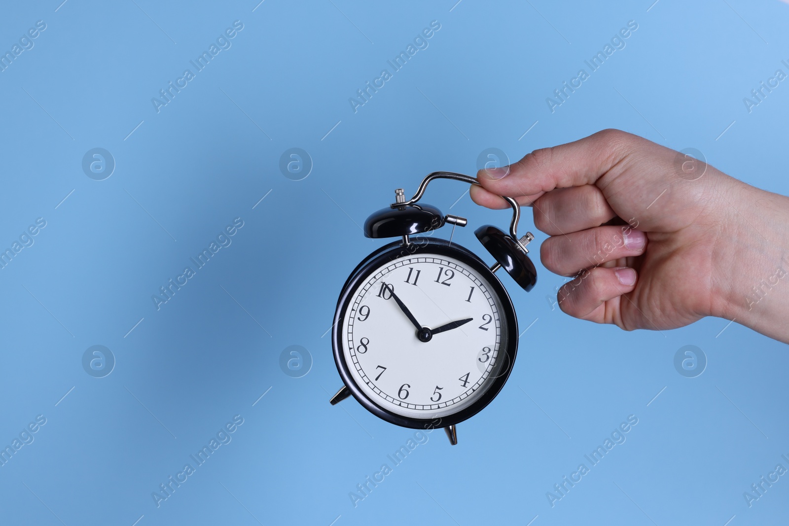 Photo of Man with black alarm clock on light blue background, closeup. Space for text