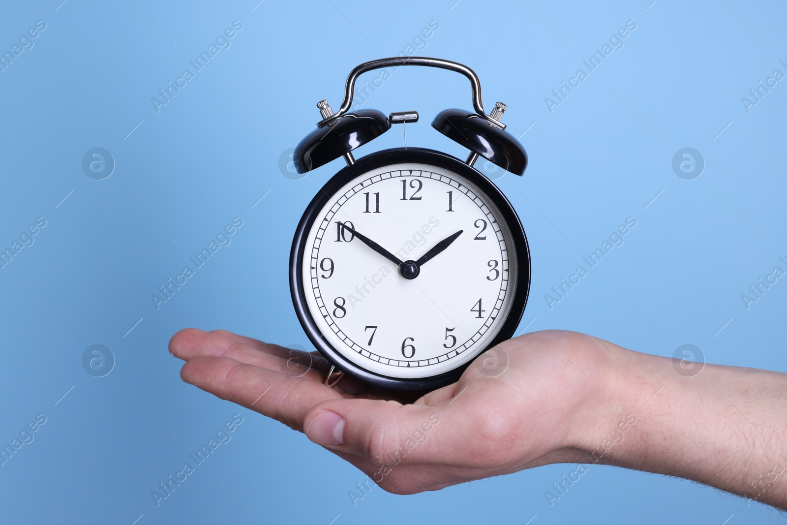 Photo of Man with black alarm clock on light blue background, closeup