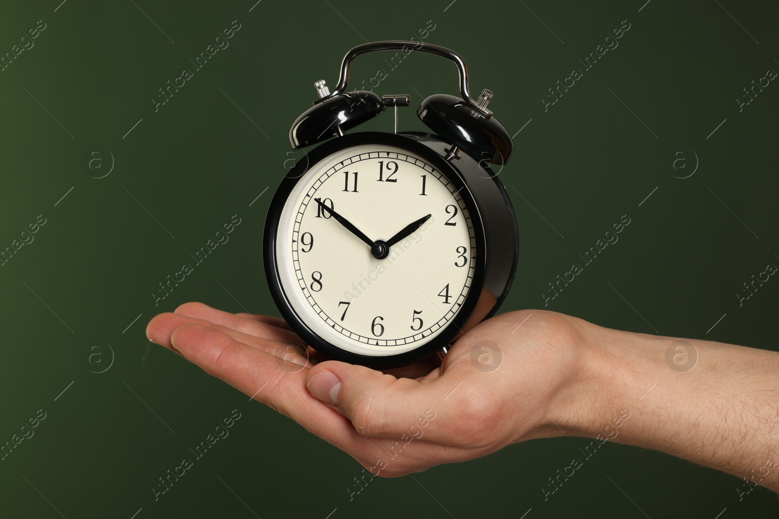 Photo of Man with black alarm clock on dark green background, closeup