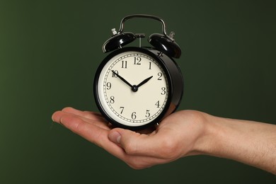 Man with black alarm clock on dark green background, closeup