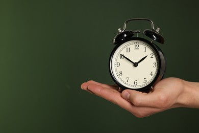 Photo of Man with black alarm clock on dark green background, closeup. Space for text