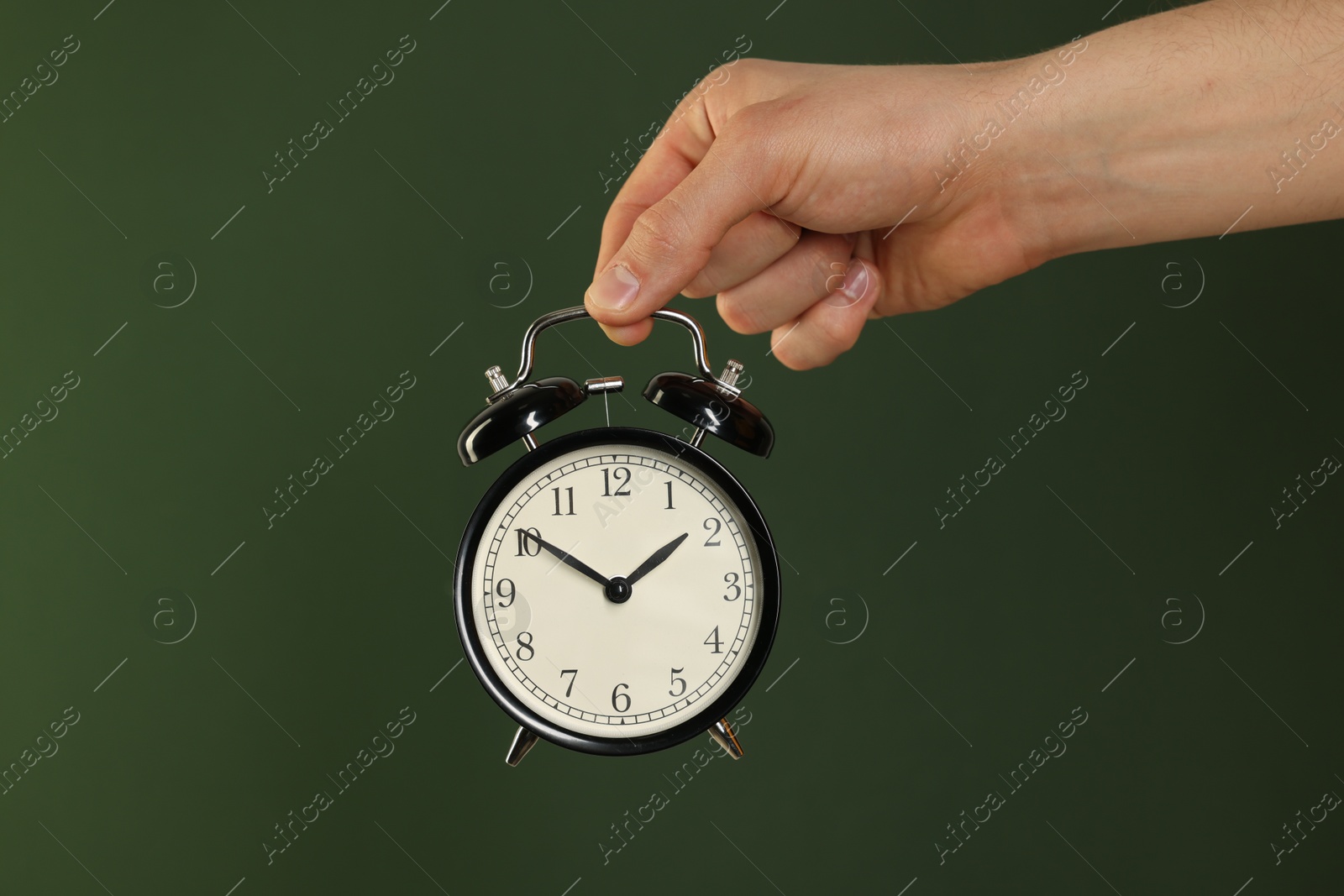 Photo of Man with black alarm clock on dark green background, closeup