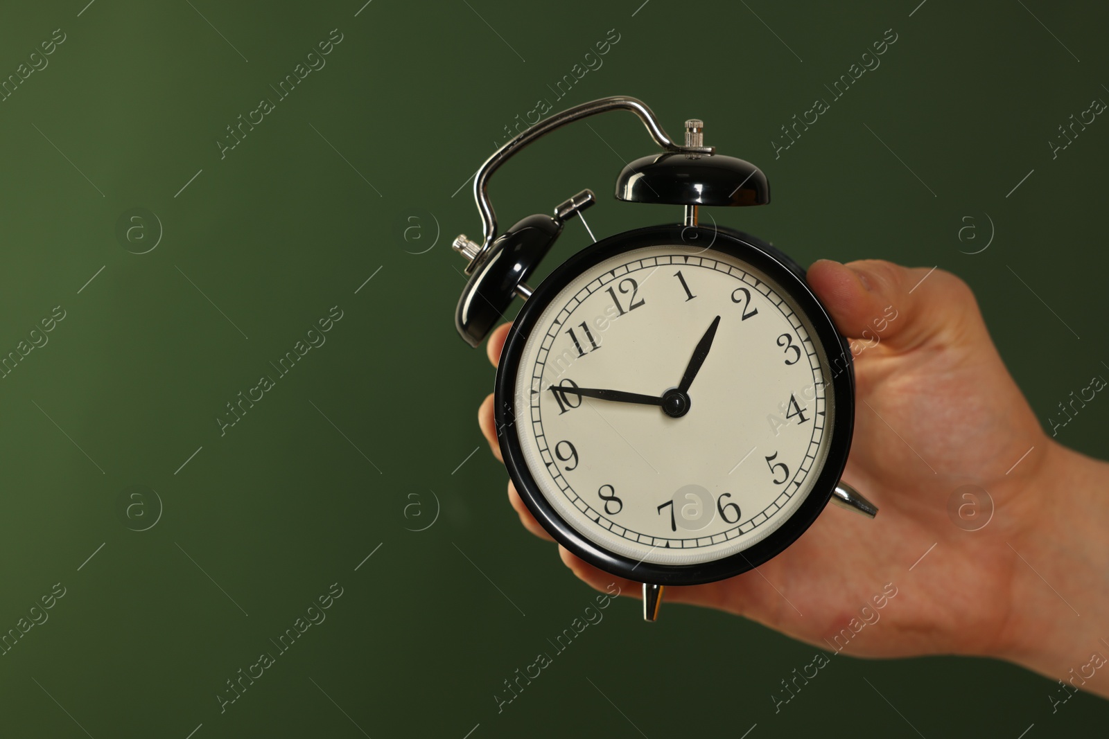 Photo of Man with black alarm clock on dark green background, closeup. Space for text