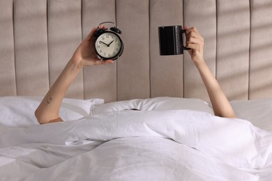 Photo of Woman with alarm clock and cup in bed at home, closeup. Good morning