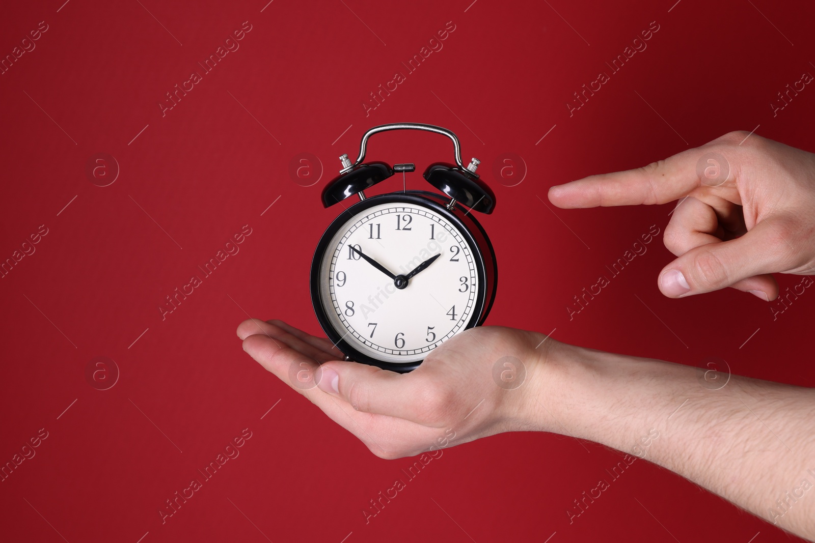 Photo of Man pointing at alarm clock on red background, closeup. Space for text