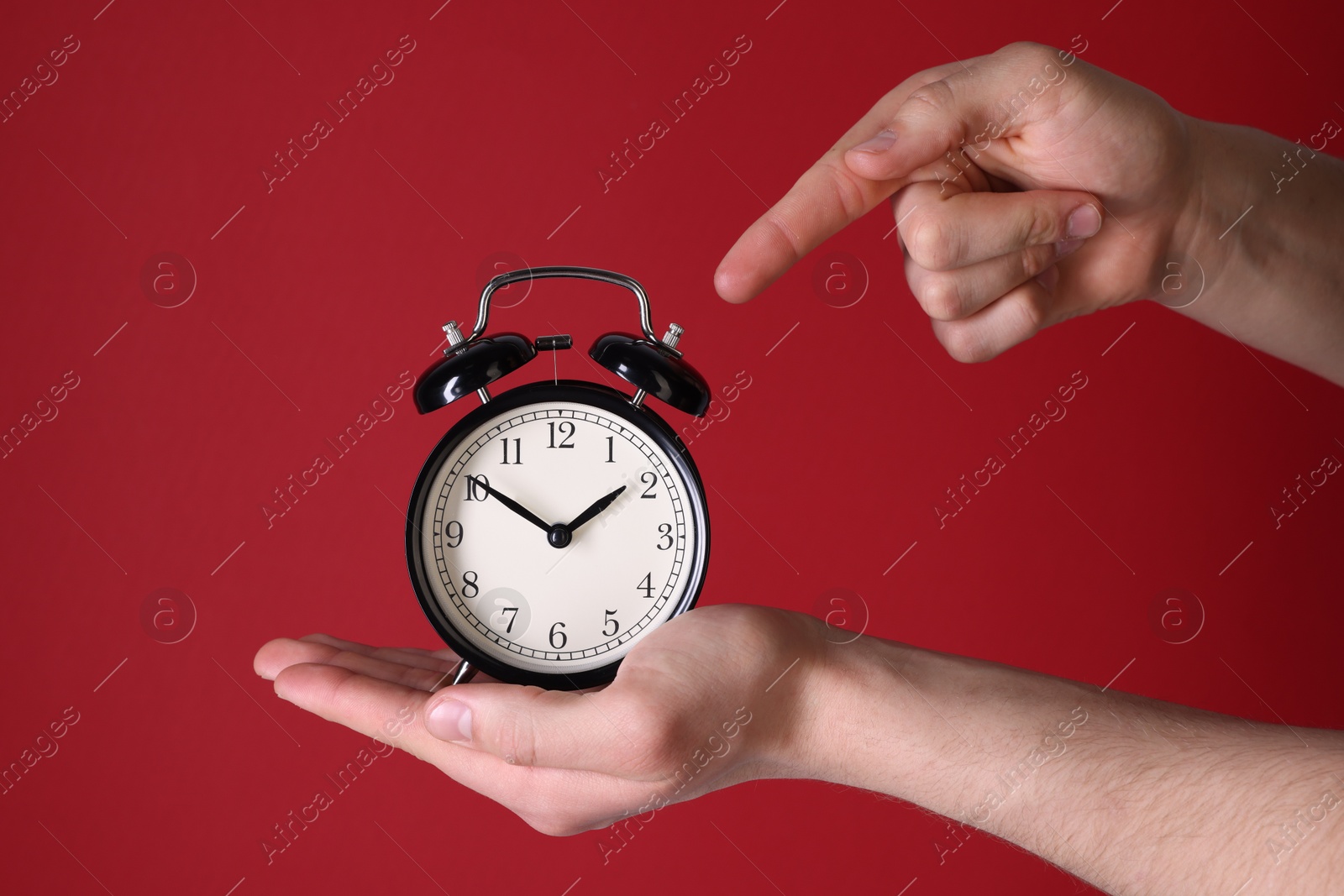 Photo of Man pointing at alarm clock on red background, closeup