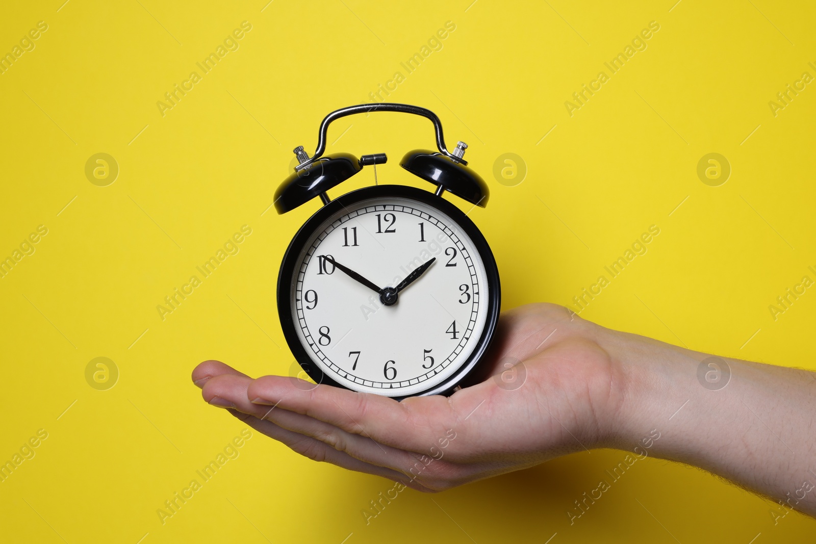 Photo of Man with alarm clock on yellow background, closeup