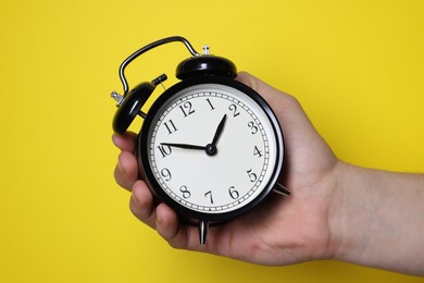 Photo of Man with alarm clock on yellow background, closeup