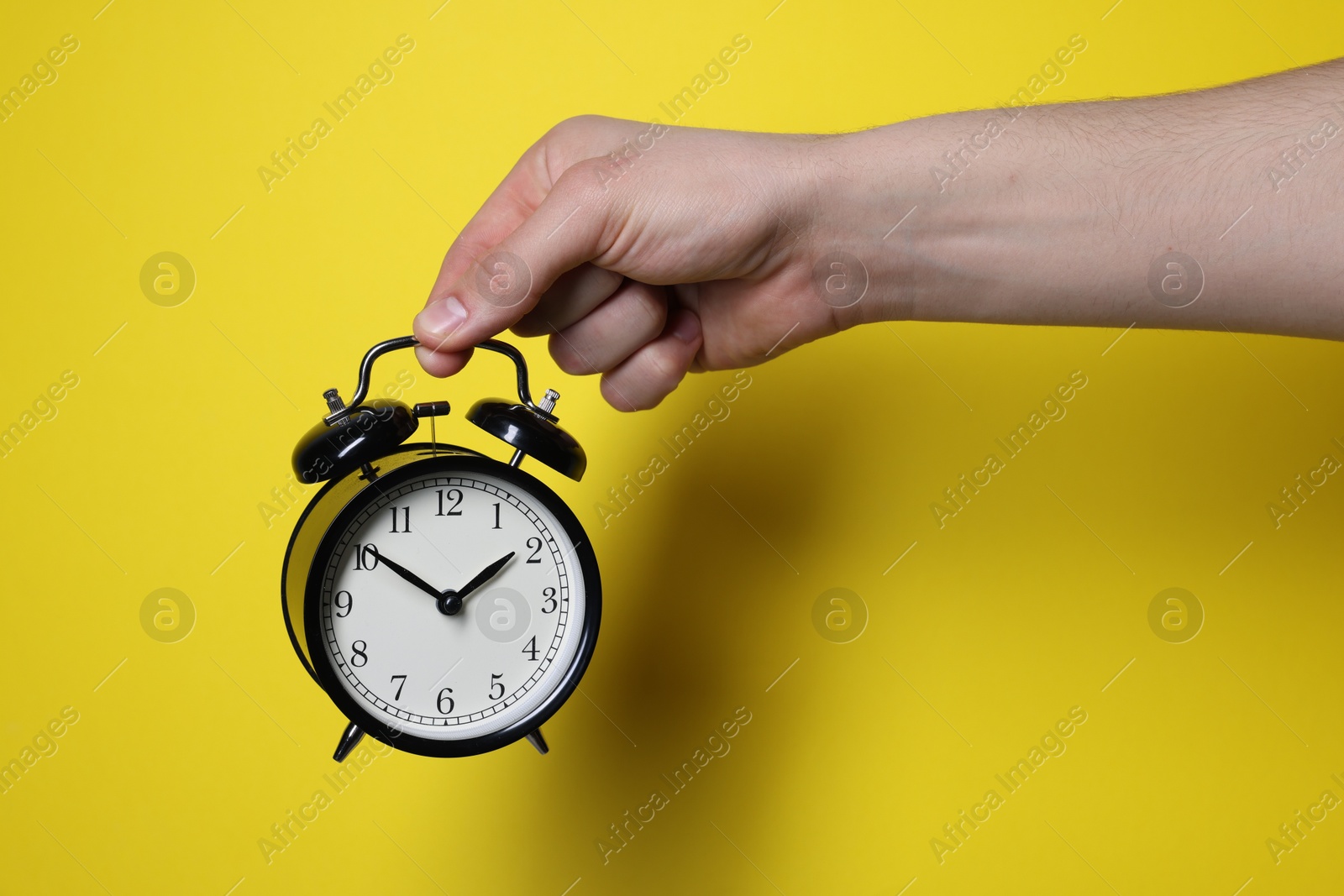 Photo of Man with alarm clock on yellow background, closeup