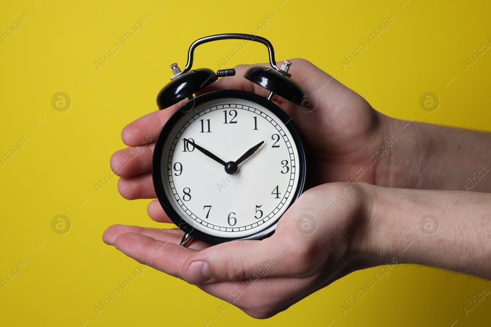 Photo of Man with alarm clock on yellow background, closeup