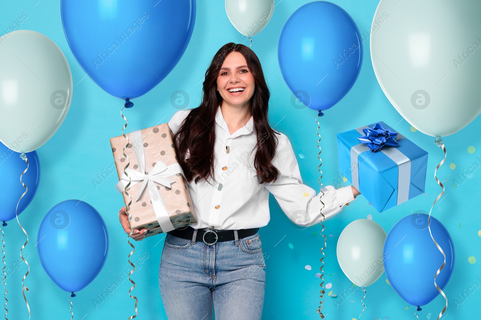 Image of Happy woman with gift boxes and bright balloons on light blue background. Surprise party