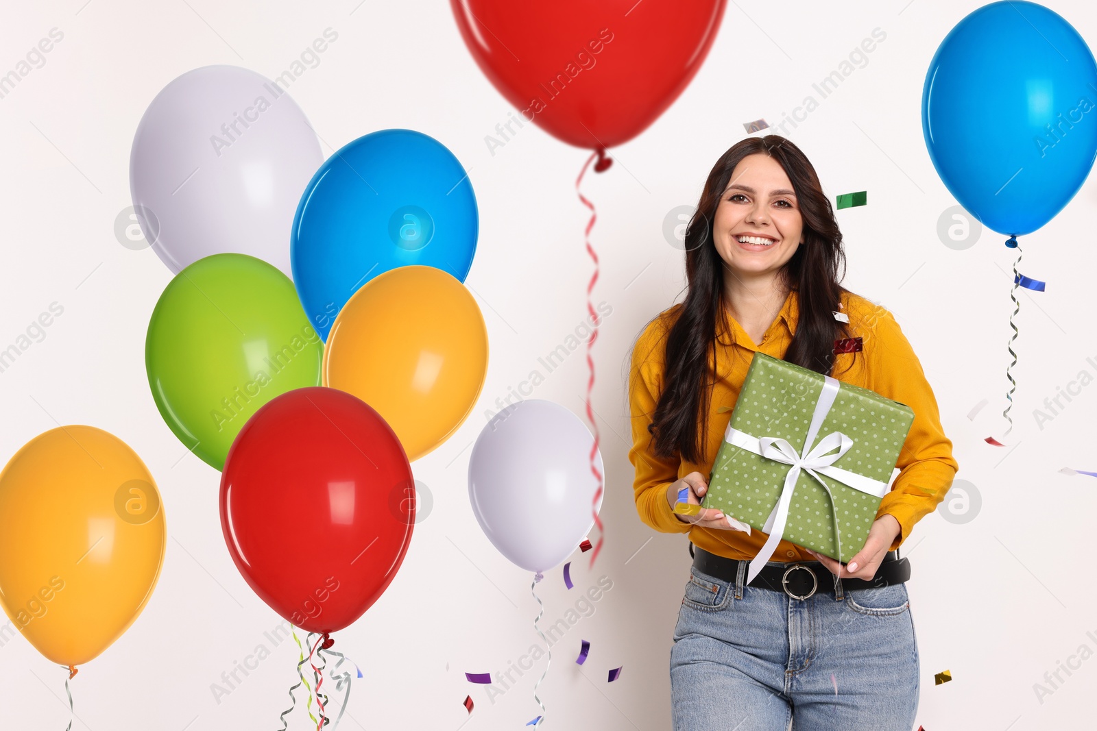 Image of Happy woman with gift box and bright balloons on white background. Surprise party