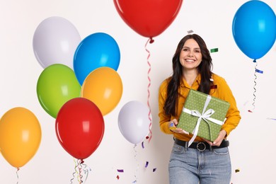 Image of Happy woman with gift box and bright balloons on white background. Surprise party