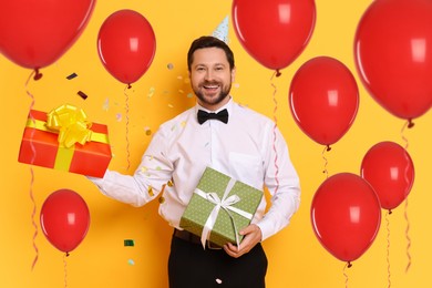 Image of Happy man with gift boxes and red balloons on orange background. Surprise party