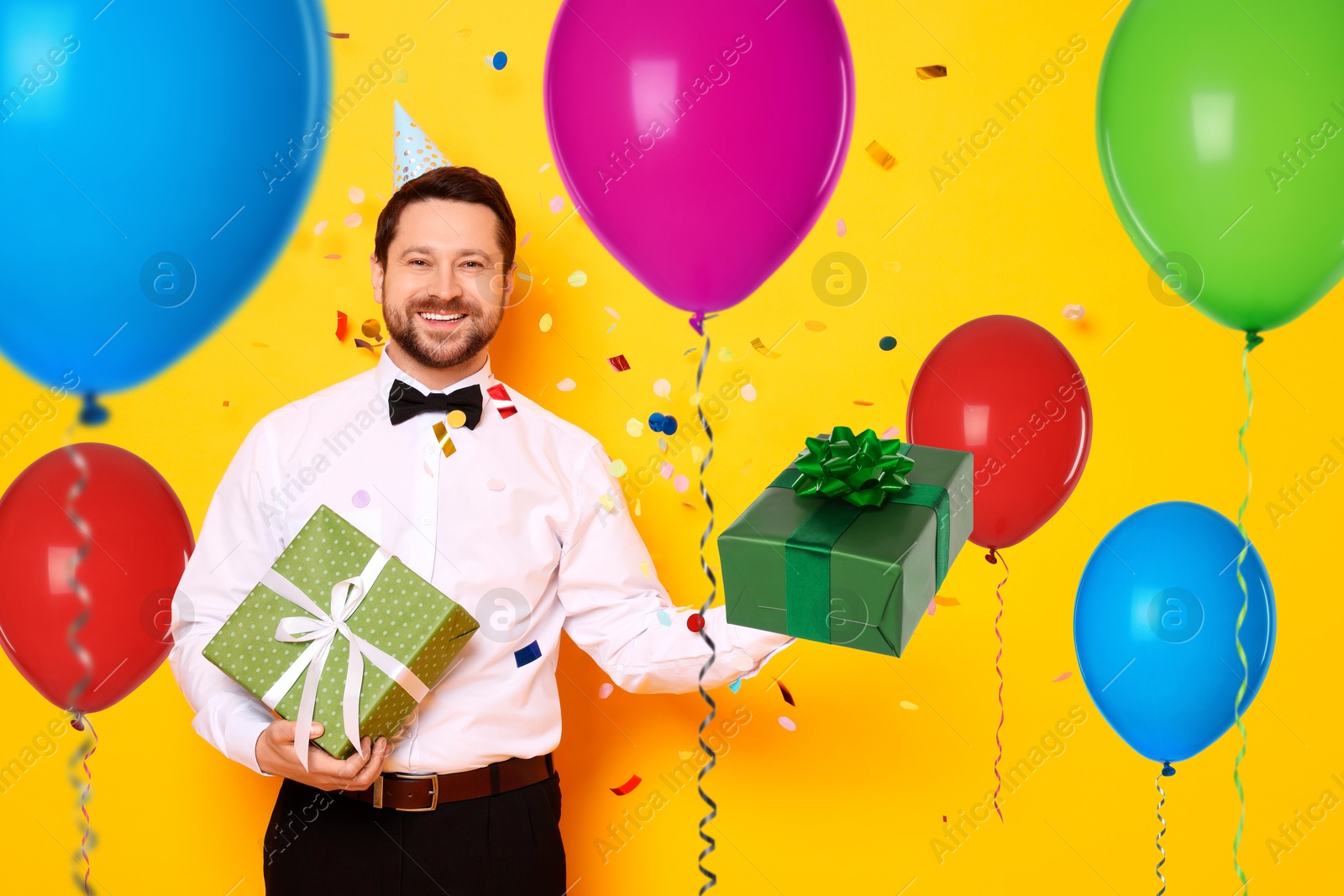 Image of Happy man with gift boxes and bright balloons on orange background. Surprise party