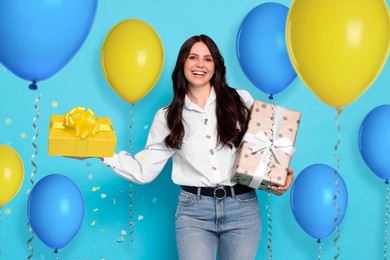 Image of Happy woman with gift boxes and bright balloons on light blue background. Surprise party